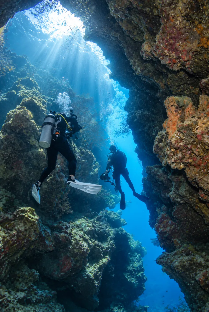Two divers in a narrow swim-through lit by sun rays at Menjangan Island